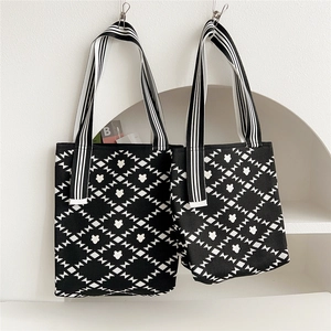 Close-up of knit tote bag featuring black and white diamond flower pattern and striped handle