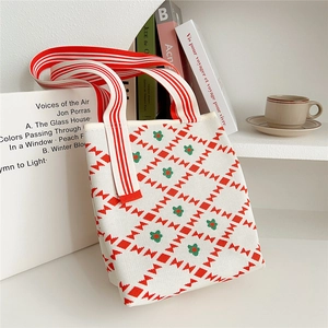Close-up of a white knit tote bag featuring red bow patterns and floral details