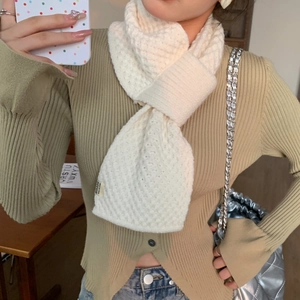 Detail of cream-white knitted cross scarf showing textured wave pattern and brand tag