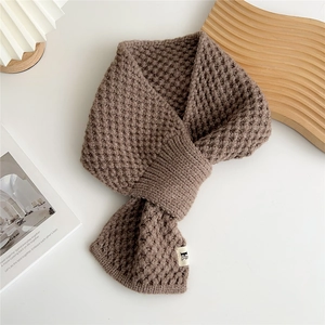 Detail of a brown waffle knit scarf with a white embroidered label on a cozy wooden tray