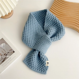 Detail of blue waffle knit scarf with a white F label on a minimalist white desk