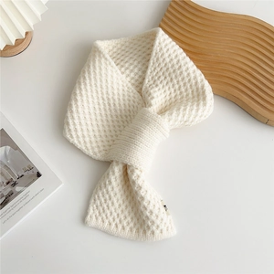 Detail of cream-white waffle knit scarf featuring cross-slot design on wooden tray