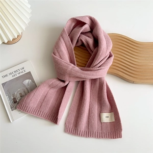 Detail of pink knitted scarf with ribbed texture and white woven label on white background