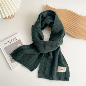 Detail of dark green knit scarf with ribbed texture and minimalist woven label branding