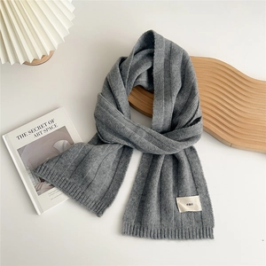 Detail view of a gray knitted scarf with vertical stripe texture and embroidered tag