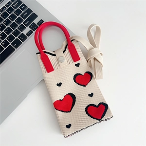 Detail of beige knitted mini crossbody bag featuring red and black heart patterns