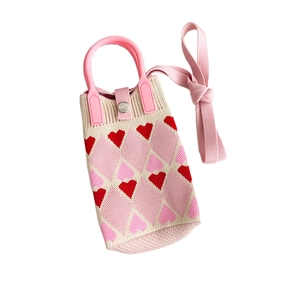 Mini knitted crossbody phone bag featuring red heart patterns and pink handles on beige fabric