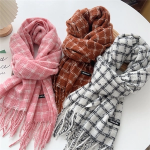 Three assorted plaid scarves with tassels and brand labels on a minimalist background