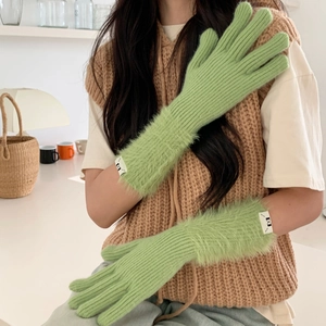 Detail of green knitted gloves featuring plush faux fur cuffs and decorative wrist label