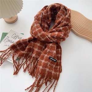 Close-up of orange plaid scarf with fringe and black brand label on a white table