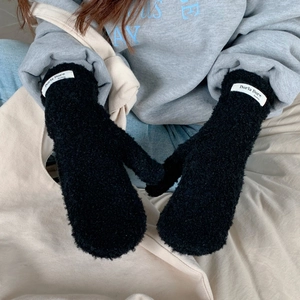 Detail of plush black mittens with branded fabric label on soft beige background