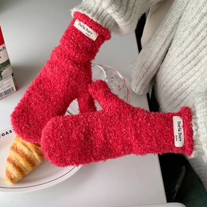 Detail of red curly plush knitted mittens featuring a stylish white woven brand label