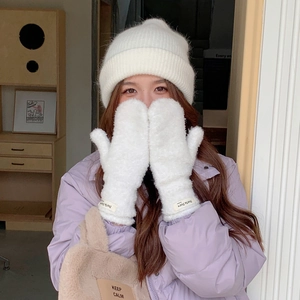 Detailed shot of white knit beanie and plush mittens set on a cozy indoor background