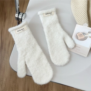Detail of white plush mittens with branded fabric label on a warm aesthetic background