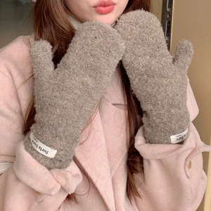 Close-up of plush taupe mittens with a white decorative tag worn on a pink coat