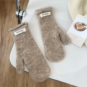 Close-up of beige fuzzy plush mittens featuring a brand label and warm sherpa texture
