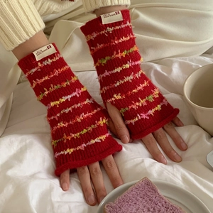 Close-up of red knitted fingerless gloves with colorful fuzzy texture on a bed
