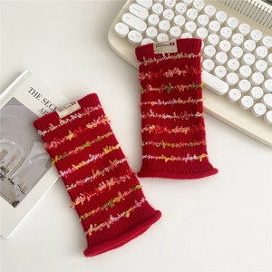 Detail of red knit fingerless gloves with colorful fuzzy stripes on a desk with a book
