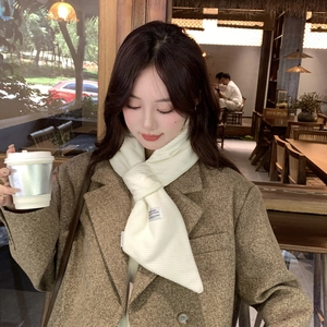 Detail of white waffle knit scarf with a cross-knot style and small woven label on brown coat