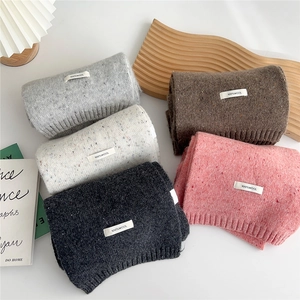 Flat lay of 100% wool knitted scarves in grey, white, tan, and pink with woven labels