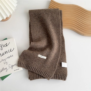 Detail of a dark brown wool knitted scarf featuring 100% wool label and ribbed edges