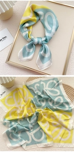Detailed close-up of patterned silk scarf with yellow and blue abstract lettering print
