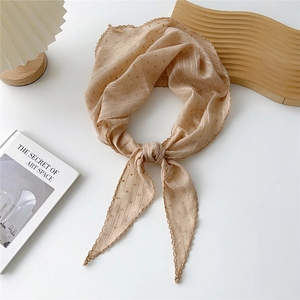 Dettaglio della sciarpa beige a righe con bordo in pizzo e pois su sfondo minimalista