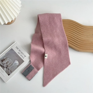 Close-up of pink knit scarf with grey stripes and woven label in a cozy home setting