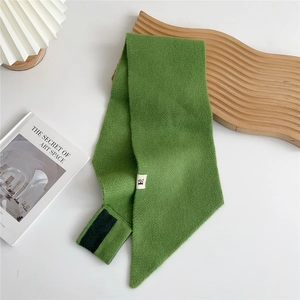 Detail of green knitted scarf with cross-hole design and white woven label on white background