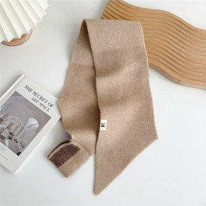 Detail of soft chunky knit scarf in beige with contrast brown trim and fabric label