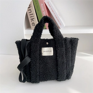 Detail of black fuzzy fleece tote bag with brand label on minimalist display shelf