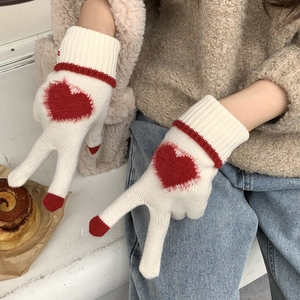 Dettaglio di guanti invernali in maglia bianca con motivo a cuore rosso e trama spessa