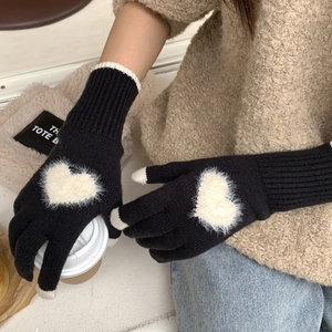 Dettaglio di guanti invernali neri in maglia con cuore di peluche bianco e touch screen