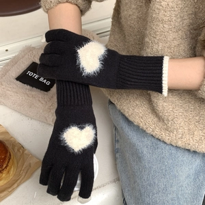 Dettaglio di guanti neri in maglia touchscreen con cuore di peluche bianco e polsini