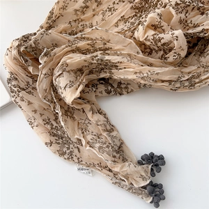 Détail d'une écharpe en coton et lin plissé avec motif floral et pompons gris décoratifs
