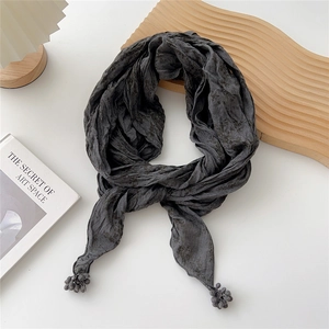 Détail d'une écharpe plissée gris foncé avec pompons sur un fond blanc minimaliste