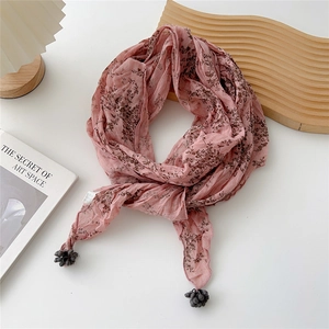 Détail d'une écharpe florale rose en coton avec pompons gris foncé et texture douce