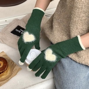 Dettaglio di guanti invernali verdi in maglia con cuore che tengono un caffè