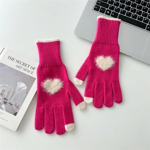 Dettaglio di guanti in maglia rosa acceso con patch a cuore soffice su una scrivania