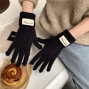 Detail of black cable knit gloves featuring a custom fabric brand label on the wrist cuff