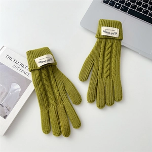 Detail of cable knit green gloves with folded cuffs and woven label on a desk
