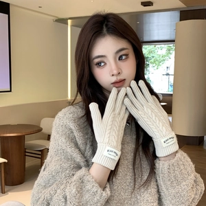 Close-up of beige knitted gloves featuring classic cable patterns and woven brand labels