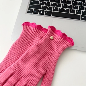 Détail de gants en maille rose avec poignets festonnés et emblème logo en métal doré