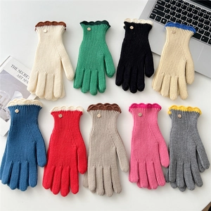 Gants en tricot multicolores avec bords ondulés contrastés et bouton sur table blanche
