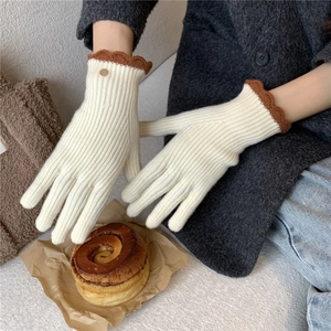 Détail de gants en tricot crème avec bordure festonnée marron et petit bouton doré