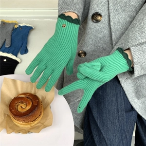 Détail de gants en tricot vert avec poignets festonnés et un bouton métallique doré