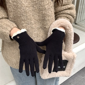 Détail de gants en tricot noirs avec poignets festonnés blancs et logo métallique