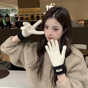 Close-up of thick beige knitted winter gloves featuring black ribbed cuffs and white labels