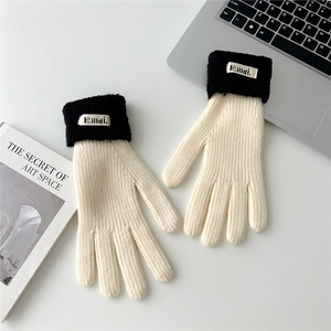 Detail of cream knitted gloves with black ribbed cuffs and brand label on a desk