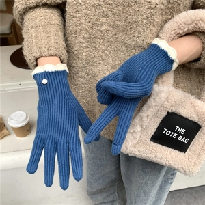 Détail de gants en tricot bleu avec bords ondulés blancs et bouton doré décoratif